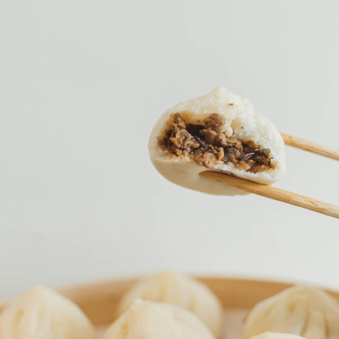 A handmade steamed bun, bitten open to show the filling, held with chopsticks