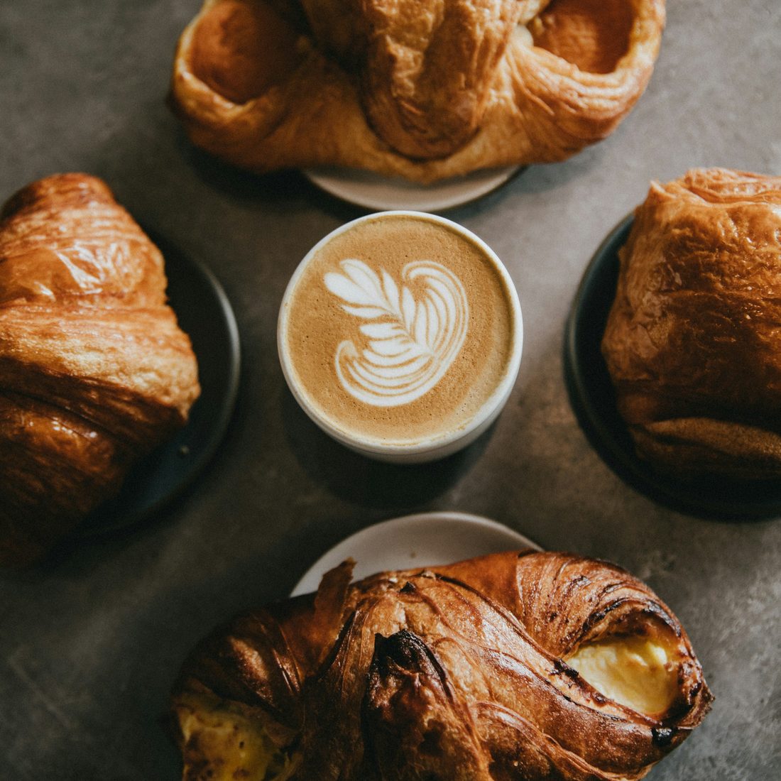Croissants and a latte with leaf-pattern art on a bakery table