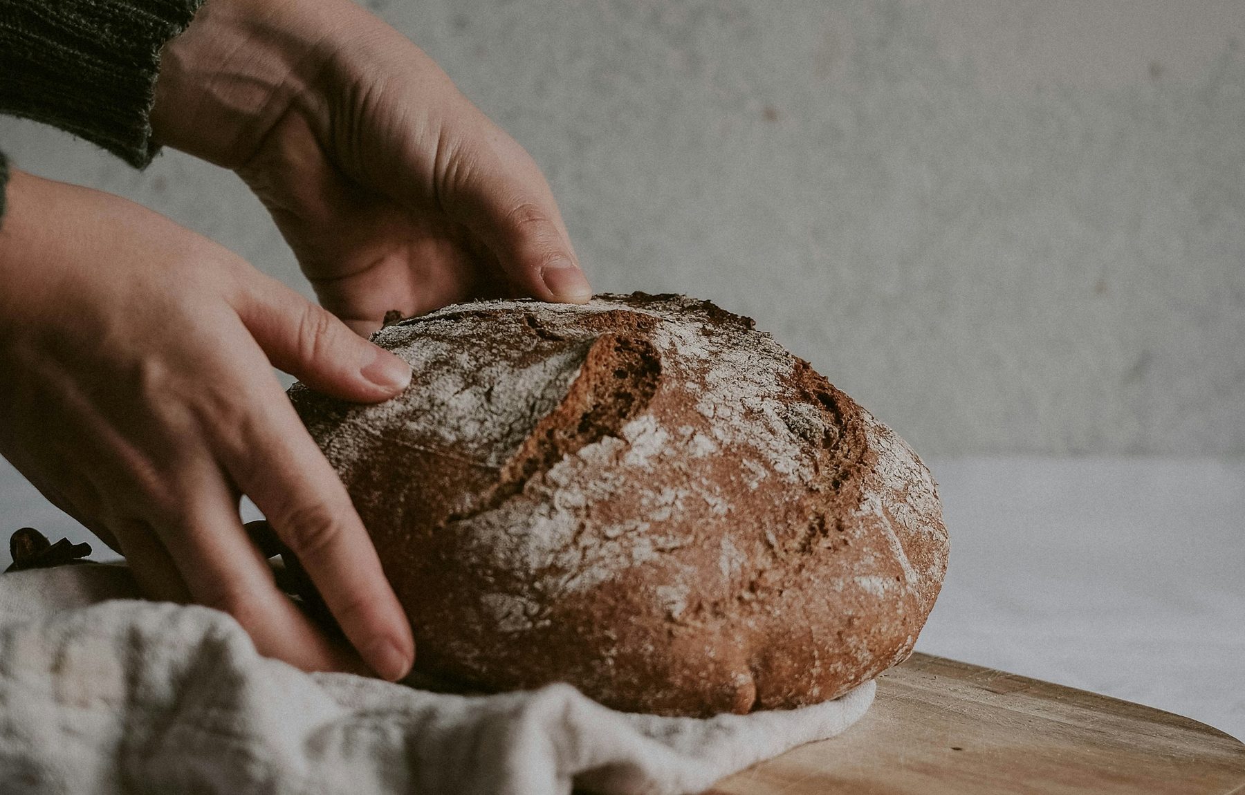 Hands lifting a freshly baked handmade loaf, dusted with flour, off the bench